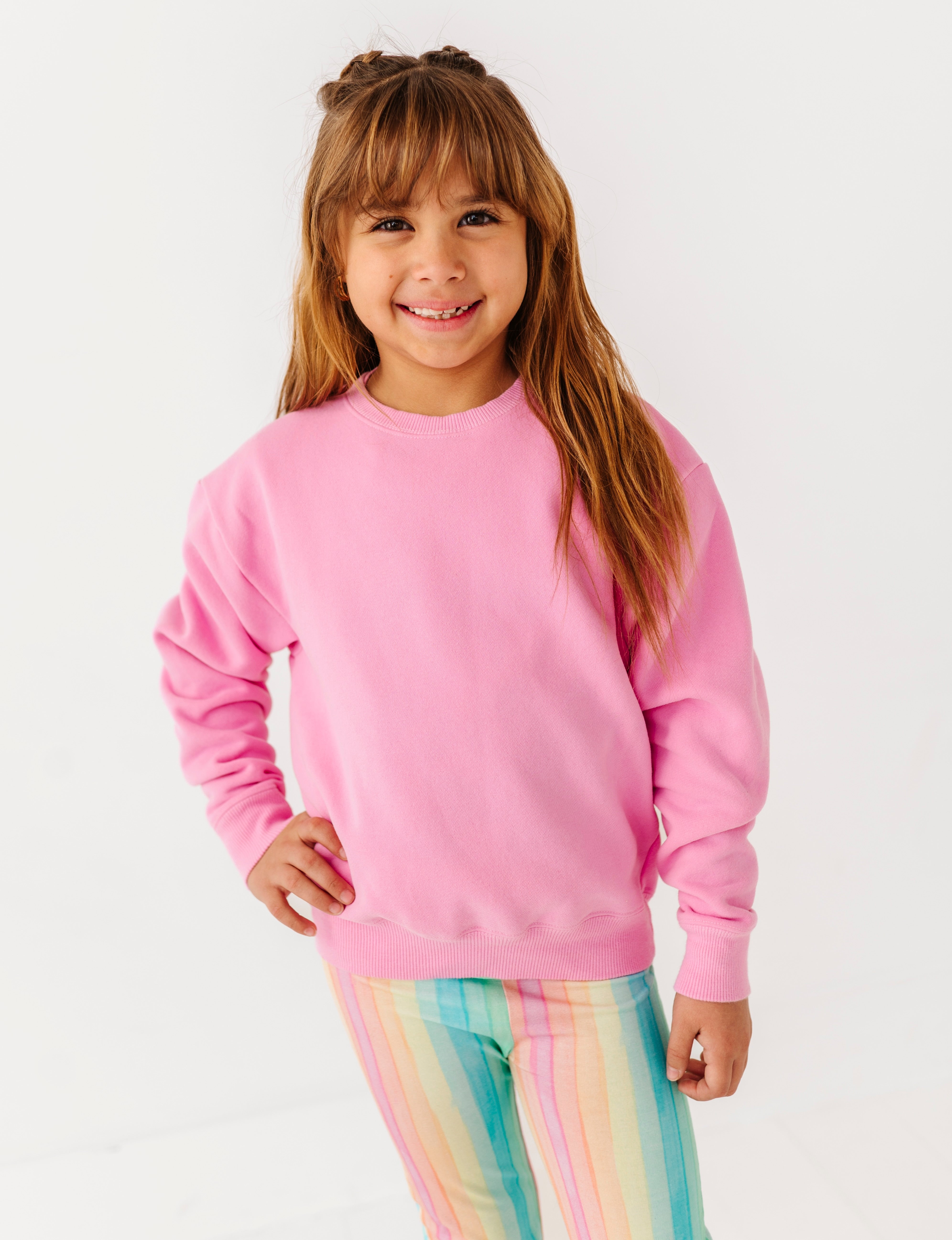 Young girl wearing a pink sweatshirt and colorful pants on a white background